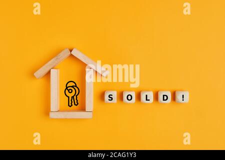 Konzept des Verkaufs oder des Kaufs eines Hauses oder einer Immobilie. Haus Symbol aus Holzblöcken und verkauft Wort auf Holzwürfeln mit Schlüssel-Symbol. Stockfoto