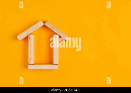 Haus-Symbol mit Holzblöcken auf gelbem Hintergrund. Flache Lay-Ansicht. Stockfoto