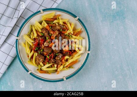 Penne Farbe Pasta mit Rindfleisch Eintopf mit Gemüse in Teller auf blauem Tisch. Stockfoto