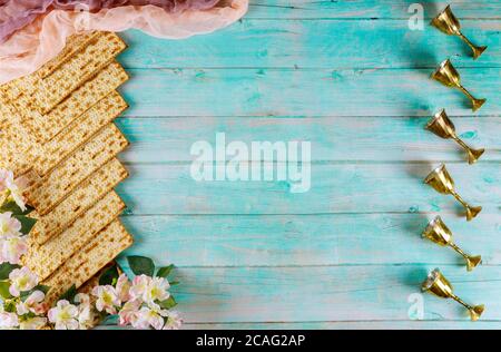 Jüdisches Matzah-Brot auf blauem Holzhintergrund mit sechs Weinbechern und Blumen. Passahfest-Konzept Stockfoto