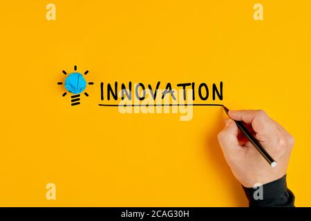 Männliche Hand schreibt das Wort Innovation neben einer Glühbirne auf gelbem Hintergrund. Konzept von Vision und Innovation. Stockfoto