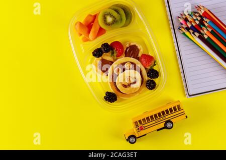 Schulspeisedose mit Pfannkuchen, frischem Obst und Schulbusspielzeug mit Vorräten. Zurück zur Schule Konzept. Stockfoto