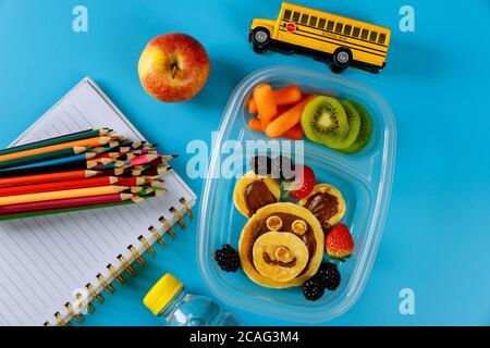 Schulspeisedose mit Pfannkuchen, frischem Obst und Schulbusspielzeug mit Vorräten. Zurück zur Schule Konzept. Stockfoto