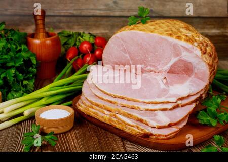 Geräucherter Schinken ohne Knochen mit Gemüse und Salz auf Holzweihnachtstisch. Stockfoto