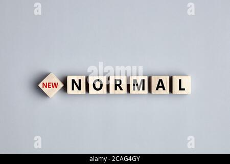 Das Wort New Normal während der Tage der Coronavirus-Pandemie ist auf Holzwürfeln auf grauem Hintergrund geschrieben. Stockfoto