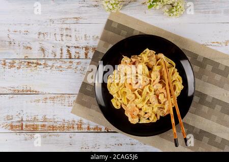 Asiatische Küche. Pasta Fettuccine mit alfredo-Sauce und Garnelen in schwarzer Platte mit Essstäbchen. Draufsicht. Stockfoto