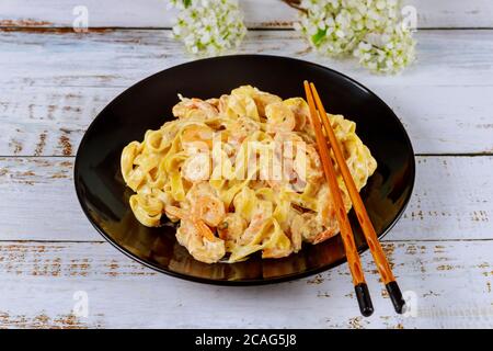 Fettuccine Pasta mit Garnelen auf schwarzem Teller mit Essstäbchen. Asiatische Küche. Stockfoto