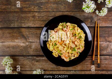 Fettuccine Pasta mit alfredo Sauce und Garnelen auf schwarzem Teller mit Essstäbchen. Stockfoto