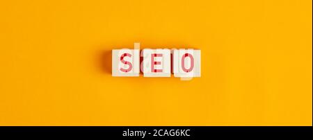 SEO (Suchmaschinenoptimierung) Buchstaben auf Holzblöcken vor gelbem Hintergrund. Flache Lay-Ansicht. Stockfoto