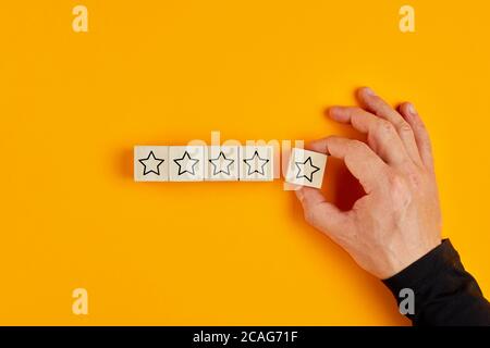 Männliche Hand Platzierung Holzwürfel mit fünf Sternen Bewertung auf gelbem Hintergrund. Konzept der Kundenerfahrung oder Zufriedenheitsumfrage. Stockfoto