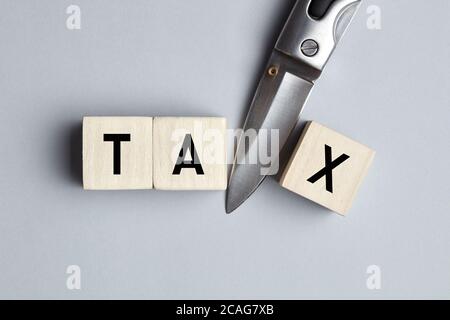 Das Wort Tax Cut auf Holzwürfel mit einem Messer geschrieben. Steuersenkungs-, Senkungs- oder Abzugskonzept. Stockfoto