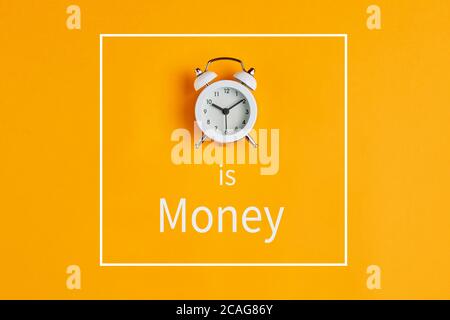 Zeit ist Geld Konzept mit Wecker und Text auf gelbem Hintergrund geschrieben. Wertvolle Ressource für das Ergebnis im Geschäft. Stockfoto