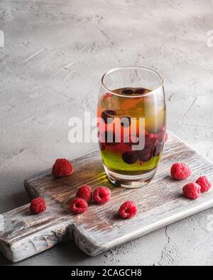 Gelee Dessert mit Beeren im Glas auf alten Holz Schneidebrett, süß bunt geschichteten Pudding, Stein Beton Hintergrund, Blick aus der Perspektive Stockfoto