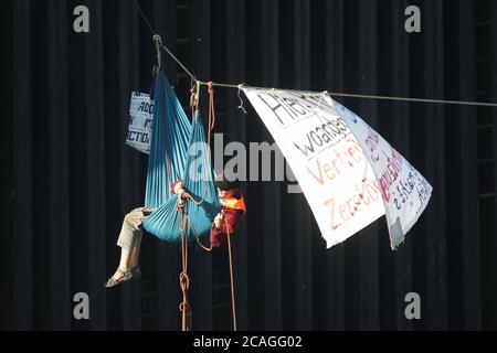 Köln, Deutschland. August 2020. Umweltaktivisten blockieren den Hafenzugang zur Shell-Raffinerie Wesseling im Rheinhafen Godorf, der zum Kölner Stadtgebiet gehört. Ein Aktivist hängt an einem Seil, das über den Hafeneingang gespannt ist. Kredit: David Young/dpa/Alamy Live Nachrichten Stockfoto