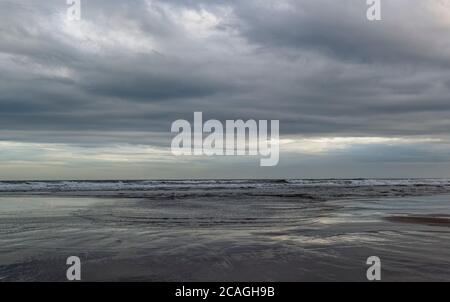 Eine Reihe von Surf kommt in den Strand von St Cyrus unter schweren Wolken von einem Sommersturm, mit kleinen Wellen von Wasser kommen den Strand. Stockfoto