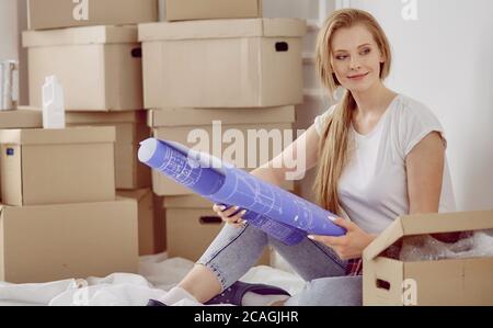 Mädchen sitzt zwischen Boxen macht Marken auf dem Plan der Wohnung Stockfoto