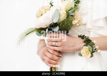 Zugeschnittenes Foto der Braut mit Ehering hält schönen Blumenstrauß isoliert über weiße Wand Stockfoto