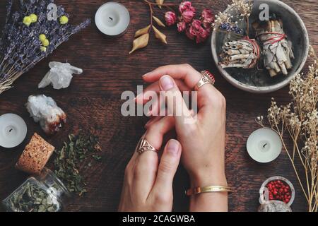 Hexen Hände auf einem Tisch bereit für Zauberarbeit. Wiccan Hexenaltar mit Salbei Wischstöcke Kräuter weißen Kerzen gefüllt. Hexe mit Händen auf dem Tisch Stockfoto