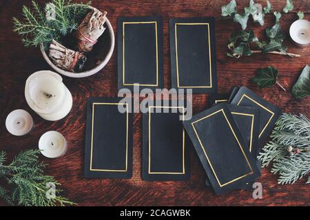 Tarot 4 Karte ausgebreitet auf einem Naturschaugerät gelegt (flaches Lay) . Handgemachte Tarot-Karten auf einem dunklen Holztisch, umgeben von Evergreens, Efeu, Salbei-Sticks Stockfoto