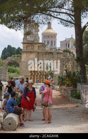 08.08.2018, Tindari, Sizilien, Italien - Touristen stehen vor den Ruinen einer antiken römischen Basilika (Gymnasium). Im Hintergrund die Kuppel von Stockfoto