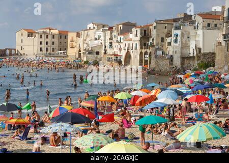 11.08.2018, Cefalu, Sizilien, Italien - Touristen und Einheimische entspannen sich am Stadtstrand unter Sonnenschirmen und baden im Mittelmeer. Im Hintergrund Stockfoto