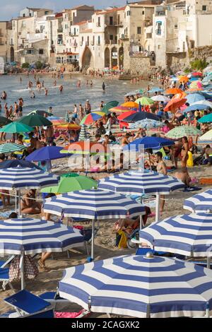 11.08.2018, Cefalu, Sizilien, Italien - Touristen und Einheimische entspannen sich am Stadtstrand unter Sonnenschirmen und schwimmen im Mittelmeer. Im Hintergrund t Stockfoto