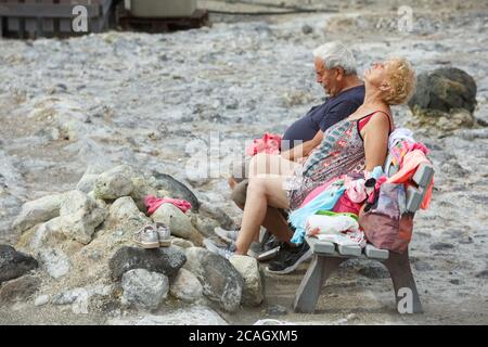 20.08.2018, Vulcano, Sizilien, Italien - ein älteres Paar sitzt mit geschlossenen Augen auf einer Bank und genießt die Wärme und Schwefeldämpfe eines Frühlings-CO Stockfoto