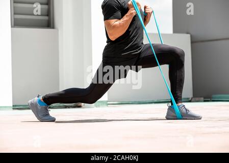 Athletischer Mann, der Ausfallschritt Workout-Übung mit Widerstand Band im Freien macht Auf dem Dach des Gebäudes in der Sonne Stockfoto