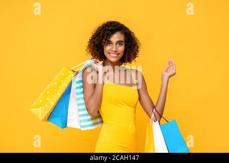 Taille bis Porträt von schönen lächelnden afroamerikanischen Frau in Modische Kleidung mit bunten Einkaufstaschen in isoliertem Studiogelb backgroun Stockfoto