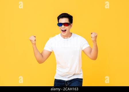 Taille bis Porträt von ekstatischen jungen asiatischen Mann trägt 3D Filmbrille schreiend und seine Fäuste isoliert auf gelb zusammenklammend studio-Hintergrund Stockfoto