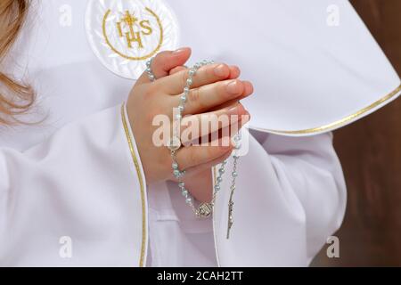 Das Mädchen der ersten Kommunion hält einen Rosenkranz in den Händen Gefaltet im Gebet und leerer Raum für Text Stockfoto