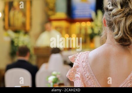 Frau sitzt in einer Kirche während einer Hochzeitsfeier gegen Ein Priester und ein junges Paar im Hintergrund und Leeres Leerzeichen für Text Stockfoto