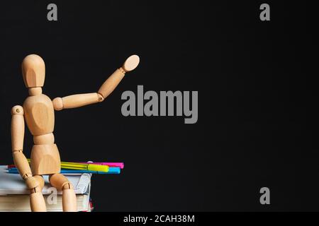 Holzpuppe sitzt auf Büchern und Büromaterial Punkte, um Platz zu kopieren. Stockfoto