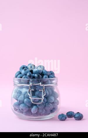 Heidelbeeren in einer offenen Glasschale auf einem rosa Hintergrund. Platz kopieren, leere Stelle für Text. Eine Beere in einem Glaskrug. Frisches Obst. Vegetarisches Konzept Stockfoto