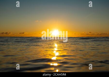 Die Sonne untergeht tief am Horizont über kleine Wellen in Manu Bay, Raglan, Neuseeland. Stockfoto
