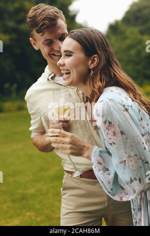 Fröhliches Paar im Park mit Champagner. Lächelnder junger Mann und Frau im Park mit Sektgläsern. Stockfoto