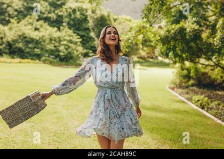 Hübsche Frau, die mit einem Picknickkorb im Park spazieren geht. Junge Frau mit einem Korbkorb beim Spazierengehen im Garten. Stockfoto