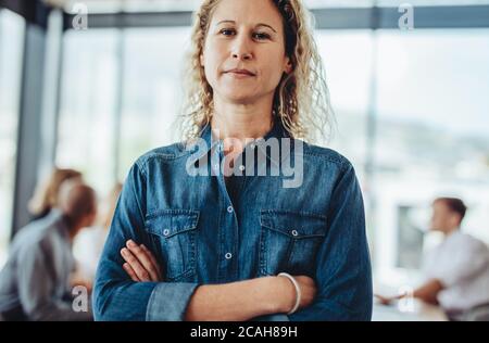 Porträt einer selbstbewussten weiblichen Geschäftsexpertin mit gekreuzten Armen. Geschäftsfrau in Casuals mit Kollegen treffen auf der Rückseite. Stockfoto