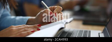 Frau im Büro sitzt am Schreibtisch und macht Notizen in Notebook. Business Stockfoto