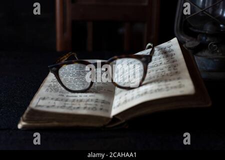 Alte getragene Gläser, die auf einem geöffneten Buch mit Büchern und Uhr im Hintergrund ruhen. Lesezeitkonzept Stockfoto