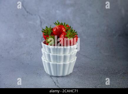 Erdbeerbeeren in einer weißen Schüssel auf einem Betontisch. Platz für Text. Erdbeeren auf einem Teller - Dessert. Gesunde Ernährung. Frühstück auf grauem Hintergrund Stockfoto