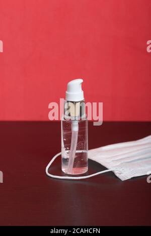 Sprühflasche mit Antiseptikum. Zur Behandlung von Händen vor Viren. Eine medizinische Maske liegt in der Nähe. Auf einem korallenen Hintergrund. Stockfoto