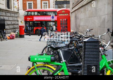 LONDON - 04. FEBRUAR 2020: Ein Leihrad mit elektrischem Leihrad in Lime, das mit normalen Fahrrädern mit einem roten Doppeldeckerbus in London, einem traditionellen roten Pho, geparkt ist Stockfoto