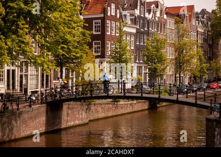 Amsterdam, Niederlande 05/15/2010: Blick auf eine Fußgängerbrücke über einen Kanal in Amsterdam. Zwei Radfahrer überqueren sie auf ihren Fahrrädern. Es gibt Tradi Stockfoto