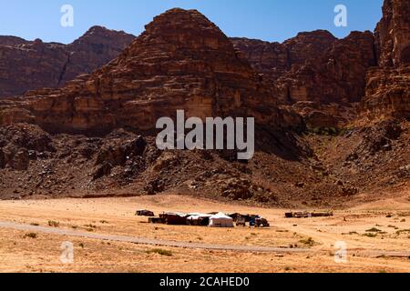 Eine kleine Gruppe von Beduinenzelten, die an einem abgelegenen Ort am Sand der Wadi Rum Desert errichtet wurden. Das Bild zeigt Zelte, Farbtöne und Geländefahrzeuge auf dem Stockfoto