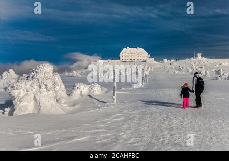 Eltern und Kinder wandern bei starkem Wind im Winter auf der Graniczna Łąka (Grenzwiese) in der Nähe der Schutzhütte in Szrenica, Nationalpark Karkonosze, Polen/Tschechien Stockfoto
