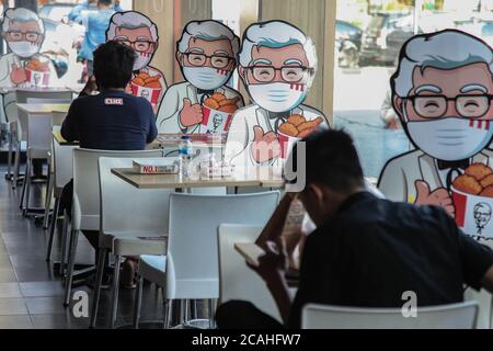 Medan, Nord-Sumatra, Indonesien. August 2020. Besucher sitzen in der Nähe von Colonel Sanders' Karton-Ausschnitt, der am 7. August 2020 auf einem Stuhl montiert wurde, um soziale Distanz in einem KFC-Restaurant in Medan, Nord-Sumatra, anzuwenden. Präsident Jokowi fragte seine Mitarbeiter, dass die Einhaltung von Gesundheitsprotokollen wie Händewaschen, Distanzhalten und das Tragen von Masken ein besonderes Anliegen sei, um die Ausbreitung des Coronavirus zu kontrollieren. Quelle: Albert Ivan Damanik/ZUMA Wire/Alamy Live News Stockfoto