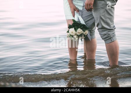 Der Blick auf das Brautpaar Beine stehen am Strand. Der Blick auf den Hochzeitsstrauß Stockfoto