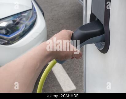 Mann, der ein Elektroauto an der Straßenstation ansteckt. Neue Energiefahrzeuge, umweltfreundliche alternative Energie für Autos Stockfoto