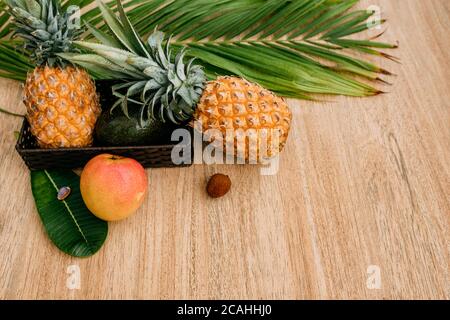 Tropische Früchte auf braunem Hintergrund mit einem schönen Palmenblatt. Ananas, Mango, Avocado, Litschi. Exotische Früchte für eine gesunde Ernährung. Kopierbereich, sp Stockfoto